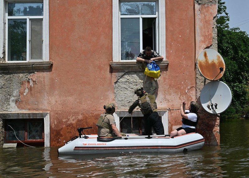 People pass a bag from a small dinghy up to a person leaning out a window.