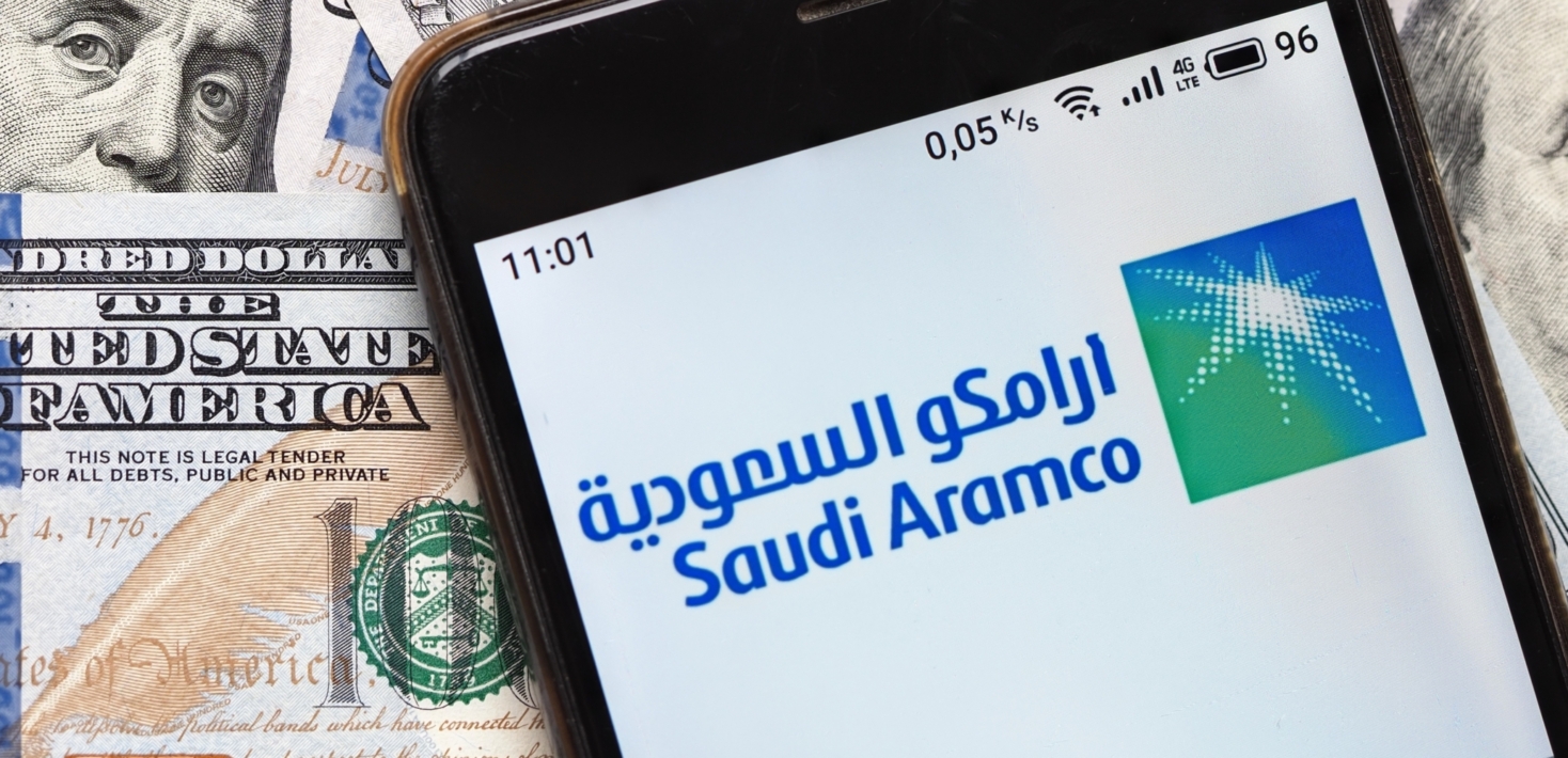 هاتف محمول يعرض شعار أرامكو ملقى على أوراق نقدية بالدولار الأمريكي