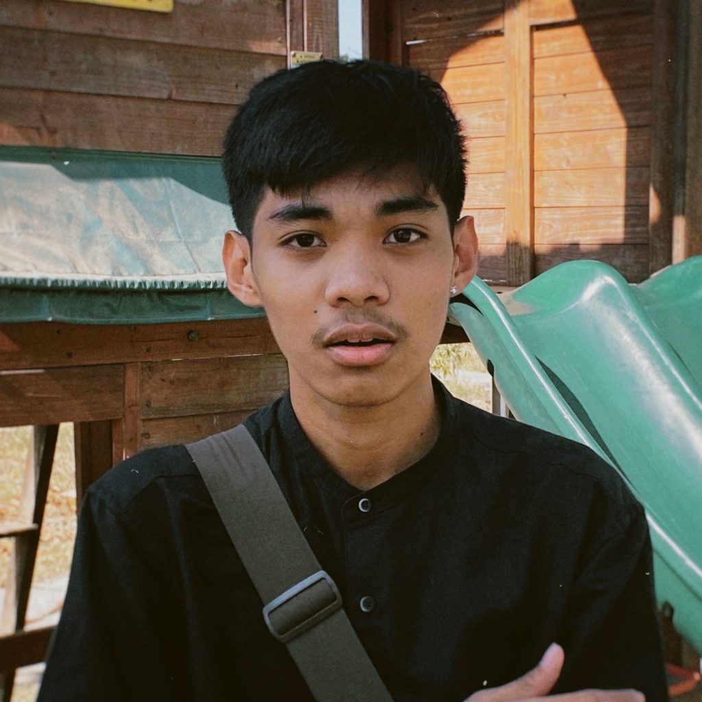 Jaime is looking directly at the camera, standing outside, wearing a black button-down shirt.