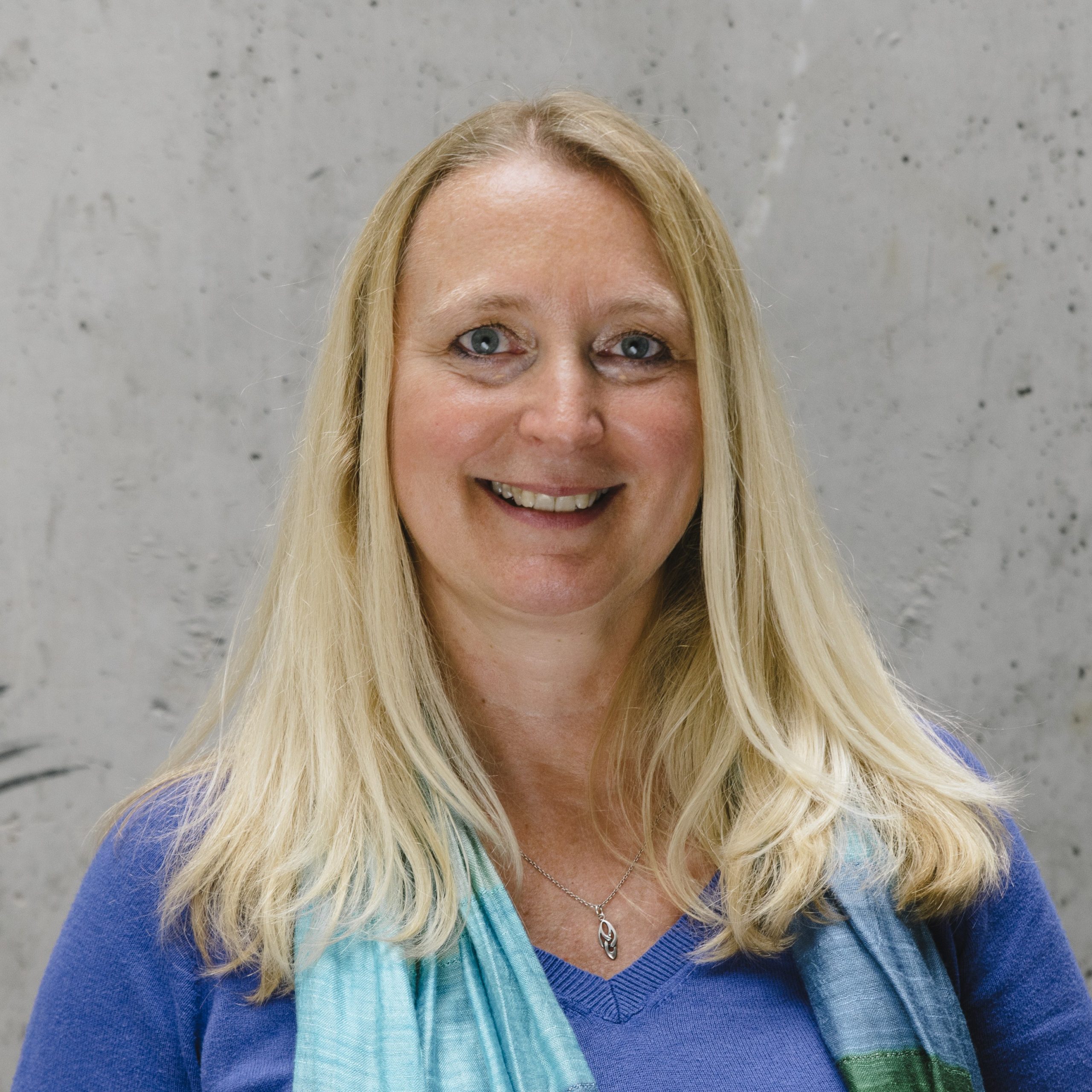 Hilde is wearing a blue top and scarf and smiling to camera.