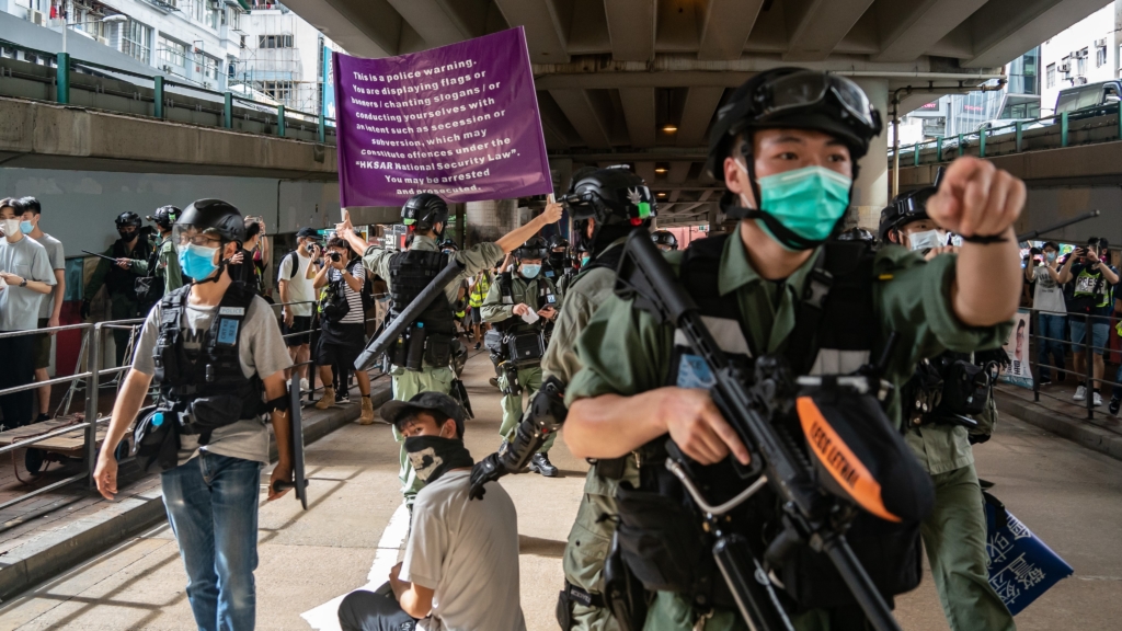 شرطة مكافحة الشغب تعتقل رجلًا بينما يحمل أحد أفرادها لافتة تحذيرية حول قانون الأمن القومي خلال تظاهرة في 1 يوليو/تموز 2020.