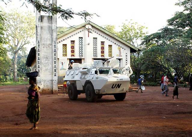 an white armoured tank sits outside a church. Several civilians walk around it 