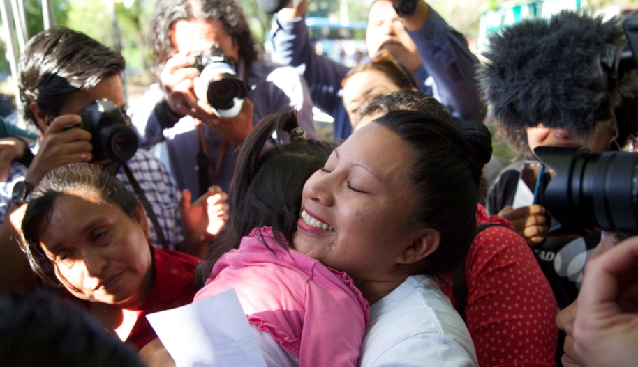 Teodora hugs her family in the middle of a large crowd of people, including photographers who capture the family's reunion. 