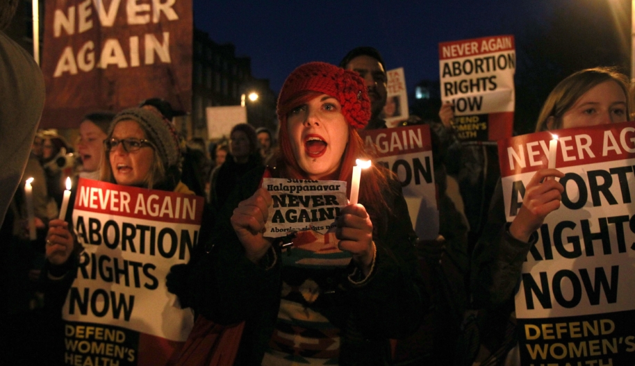 a group of women in ireland attend a candlelight vigil and hold signs that read Abortion Rights now and Never Again. 