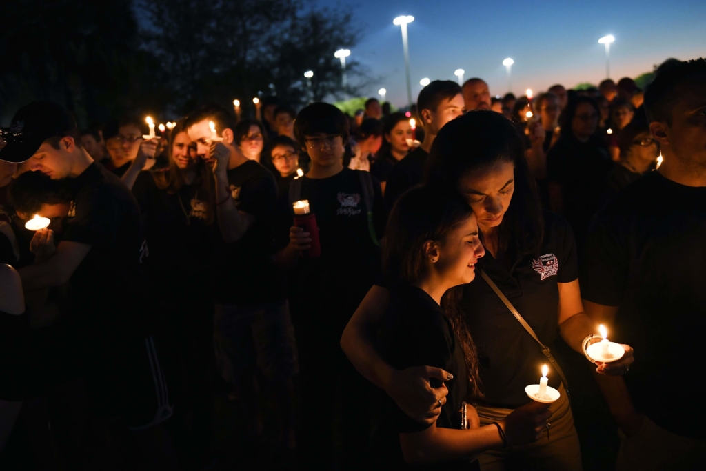 a group of mourners gather in honour of the victims of the Parkland shooting in Florida, USA. Many of them are holding candles 