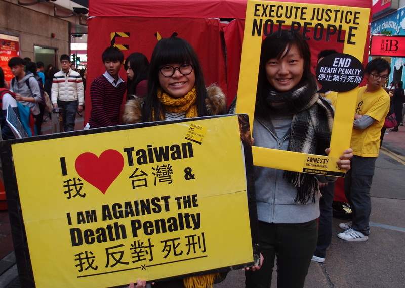 two people stand posing with signs that read 'I am against the death penalty' and ' execute justice, not people'