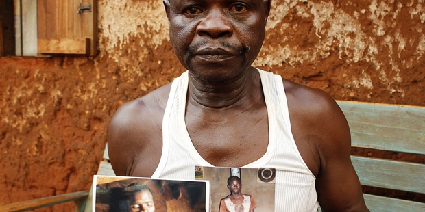 The father of Constant Yaonomo, 24, showing a photo of his dead son and of a younger son who was injured by a grenade in the same attack.