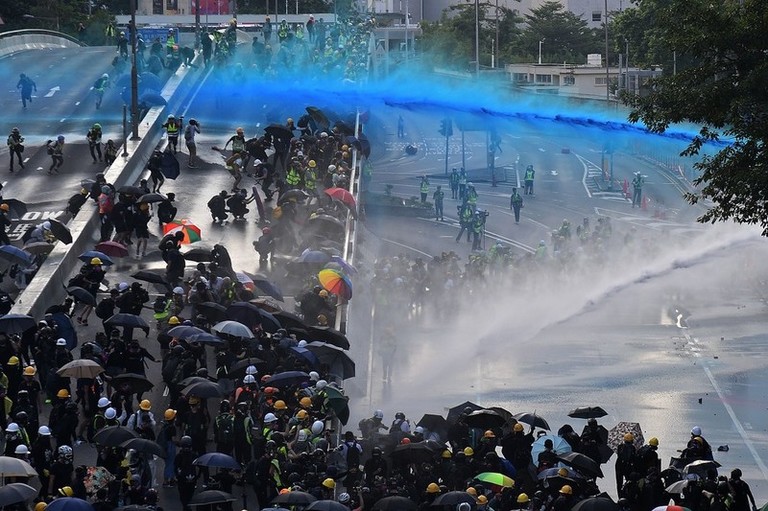 Pro-democracy protesters react as police fire water cannons outside the government headquarters in Hong Kong on September 15, 2019. - Hong Kong riot police fired tear gas and water cannons on September 15 at hardcore pro-democracy protesters hurling rocks and petrol bombs, in a return to the political chaos plaguing the city.