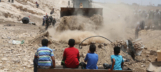 Palestinian children watch a bulldozer clearing rubble.