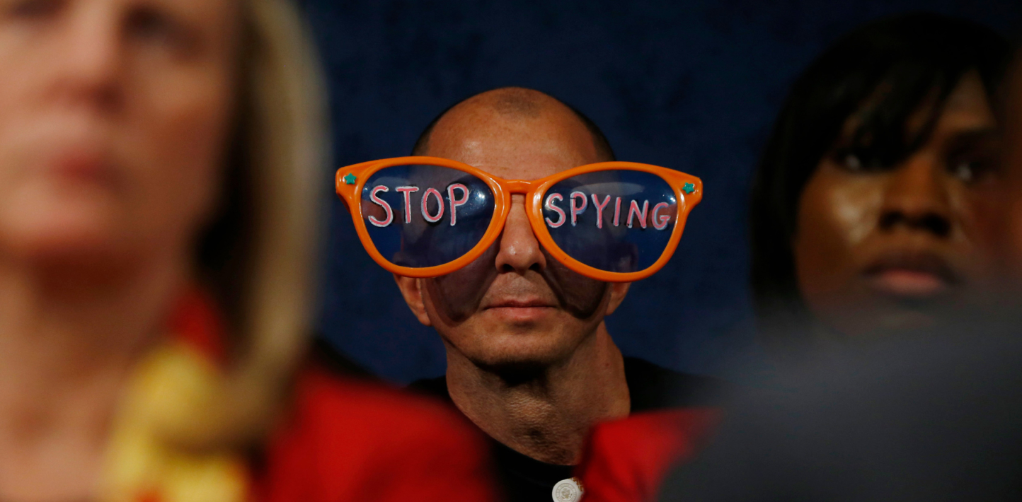 an image of someone at a protest wearing large clown glasses that say 'Stop Spying'