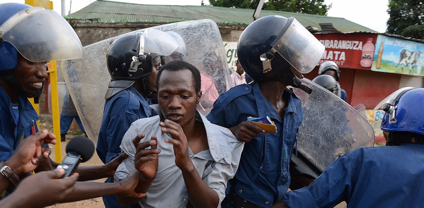 Image showing a young man in surrender as he is confronted and being dragged by four heavily armed police officers.
