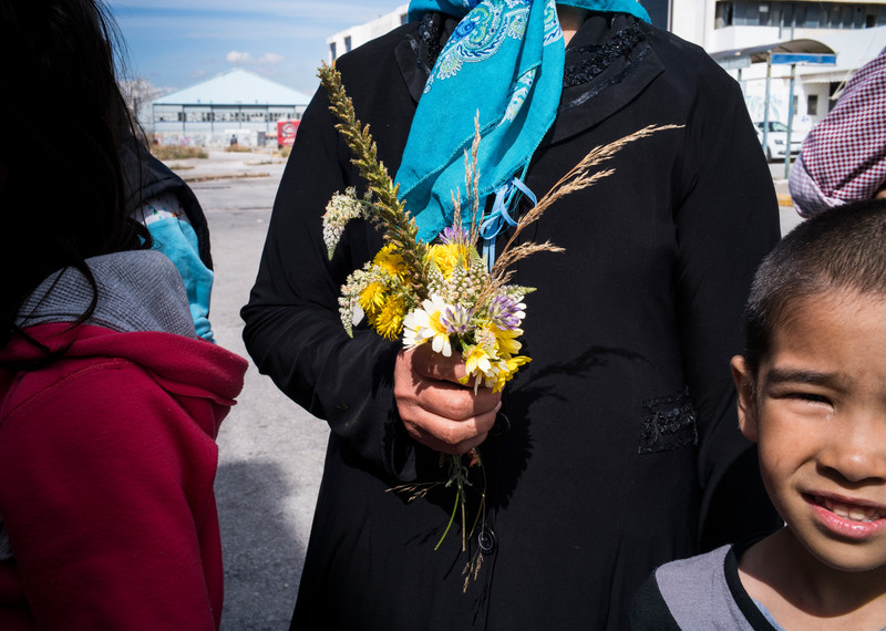 Outside the old Athens airport terminal, children run free as cars whiz past. Fawzia, a woman in a blue headscarf, is picking flowers – a touch of beauty amid the rubbish and ageing concrete. © Amnesty International/Olga Stefatou