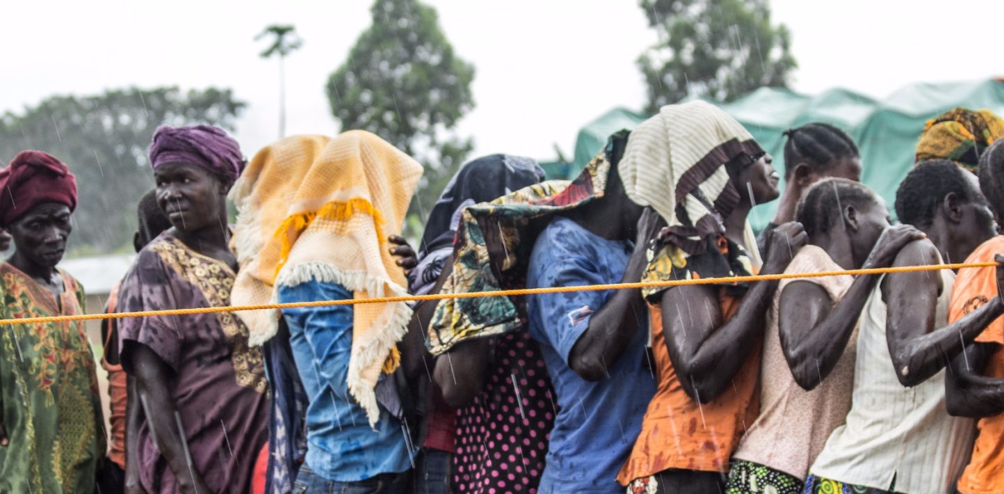 Image of women standing in a queue and shielding their heads from slight drizzle.