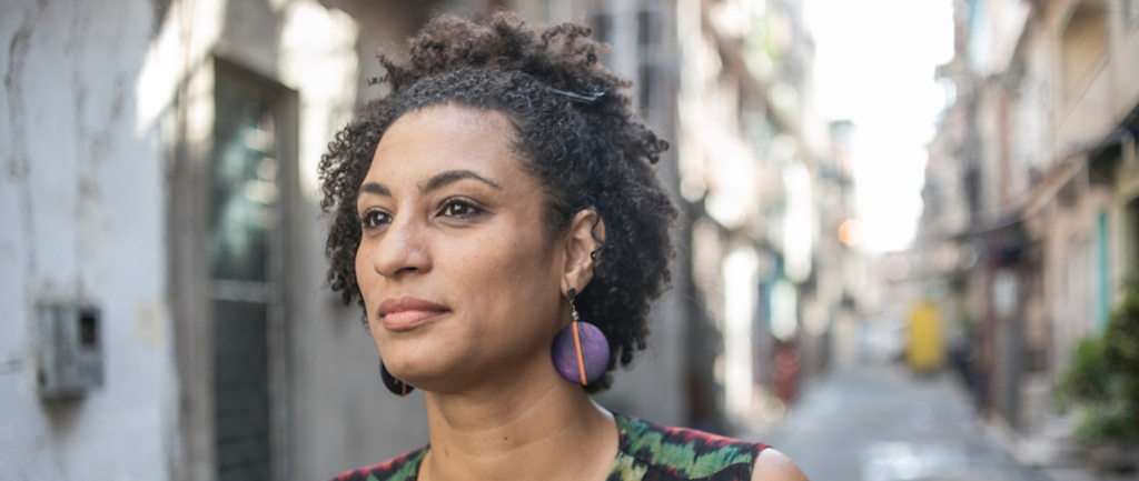 a portrait of Marielle Franco. She stares intently to the right of the camera. She is wearing purple earrings