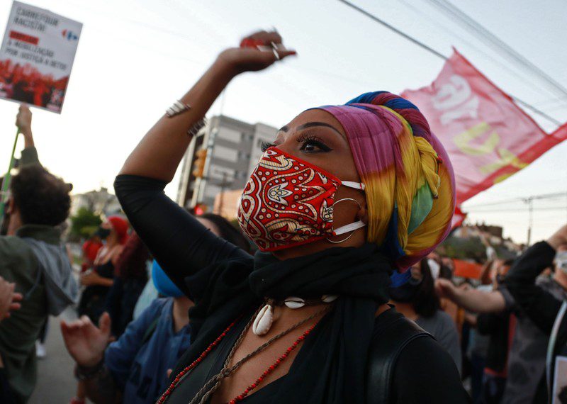 A person wearing a face mask raises her fist in the air, surrounded by other protesters.