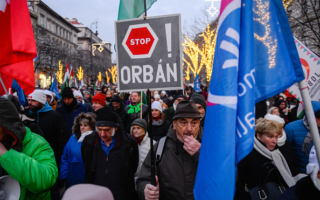 People at a protest march hold banners. In the centre of the image a man holds a banner which reads 'STOP ORBAN!'