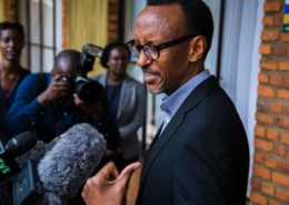Man standing with his back against a brick wall (president Paul Kagame) speaking to journalists