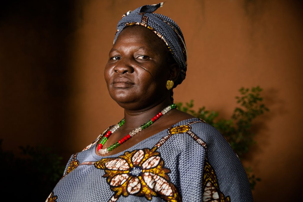 a portrait of Adama. She is wearing a headscarf and dress with a matching blue, brown and white pattern. 