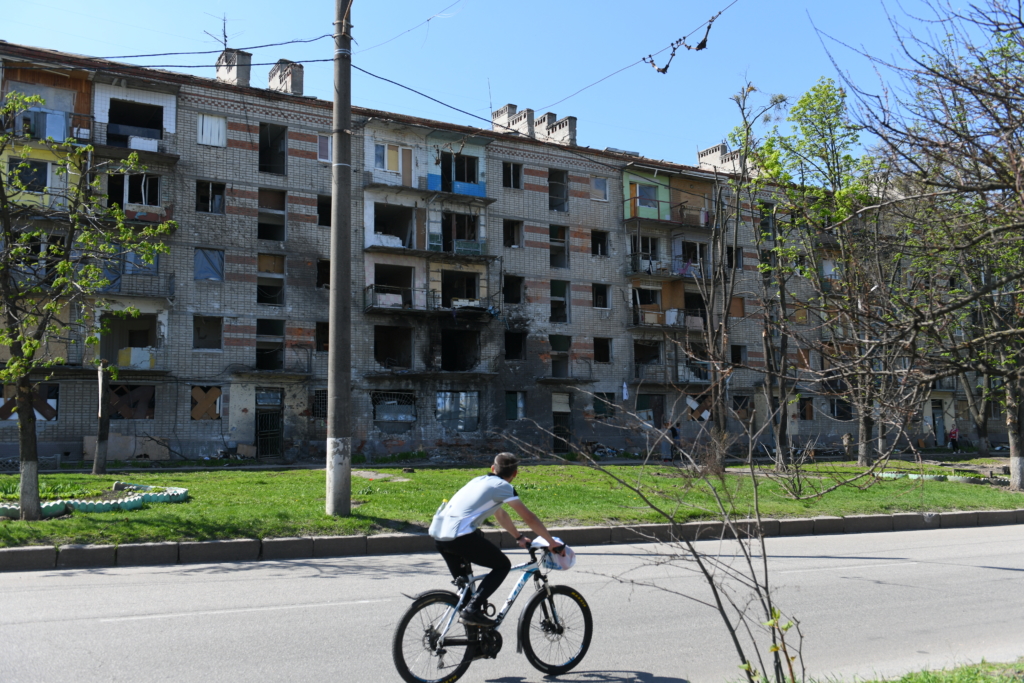 Man cycling pas buildings damaged by shelling in Kharkiv.