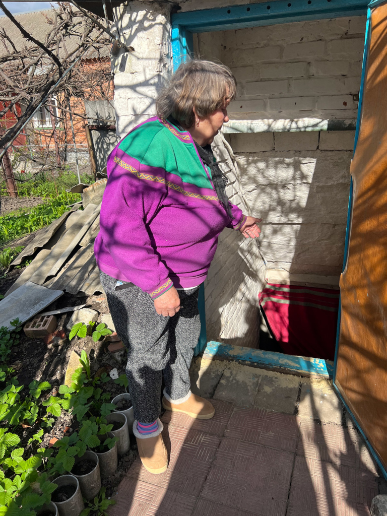 Oleksandra Andriivna by the stairs to the cellar in their garden, where her brother Viktor Andriiovych was mortally wounded by cluster munition shrapnel.