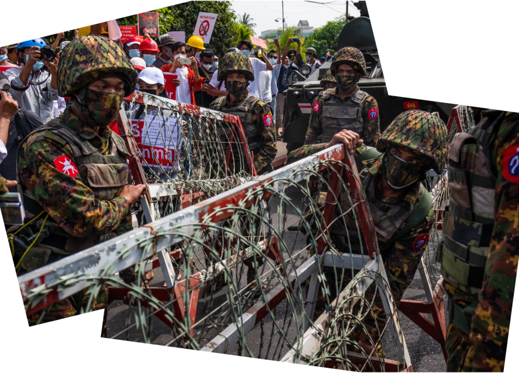 Des policiers en tenue de camouflage et masqués installent des barricades couvertes de fil barbelé. En arrière-plan, on peut voir des manifestant·e·s portant des pancartes