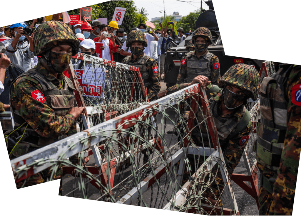 Des policiers en tenue de camouflage et masqués installent des barricades couvertes de fil barbelé. En arrière-plan, on peut voir des manifestant·e·s portant des pancartes