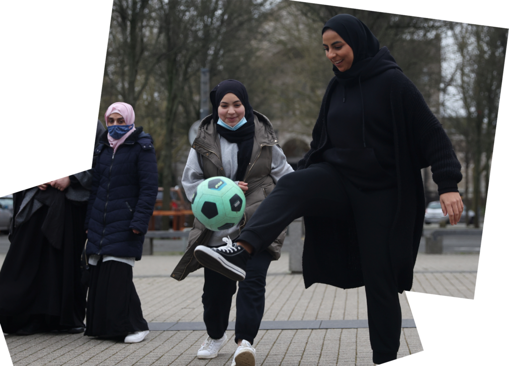 مجموعة من النساء، يرتدين جيمعن الحجاب، يركلن كرة قدم خضراء وسوداء. يبدوْن مبتهجات وهن يلعبن.