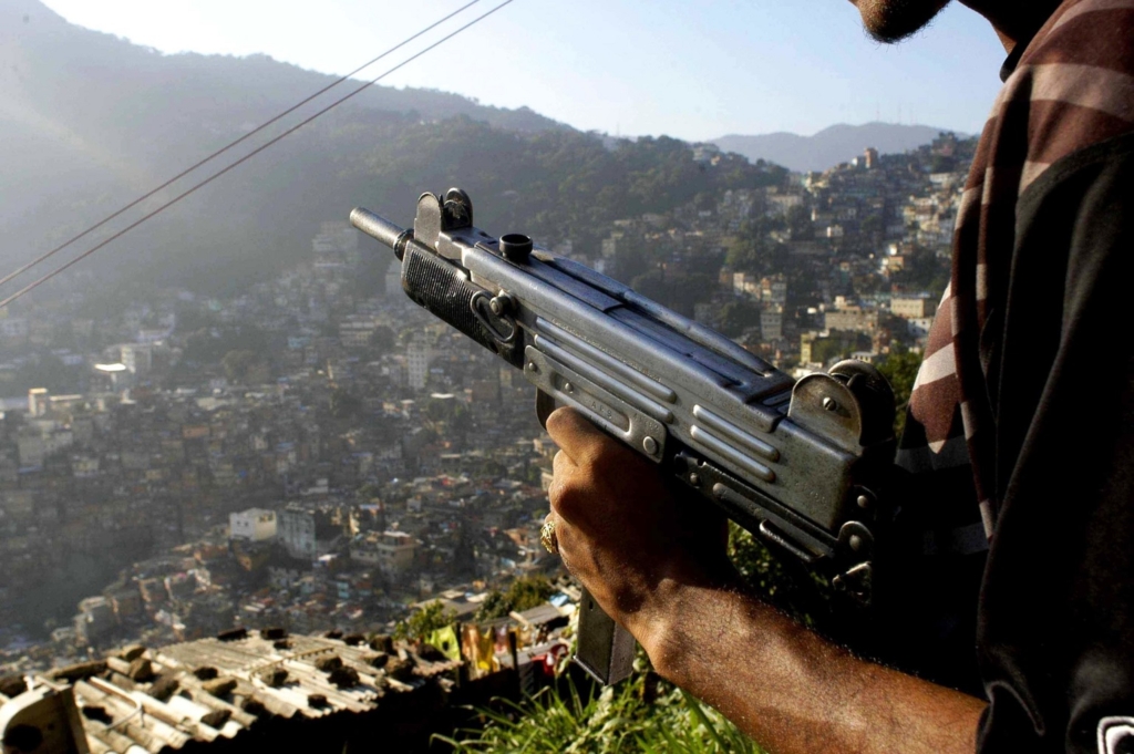 a soldier holing a submachine gun infront of a backdrop of a hilly landscape covered in buildings