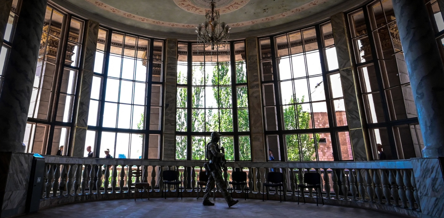 A Russian soldier patrols in front of wide tall windows in the Mariupol Philharmonic Hall..