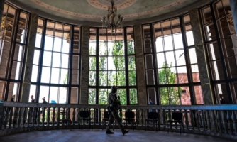 A Russian soldier patrols in front of wide tall windows in the Mariupol Philharmonic Hall..