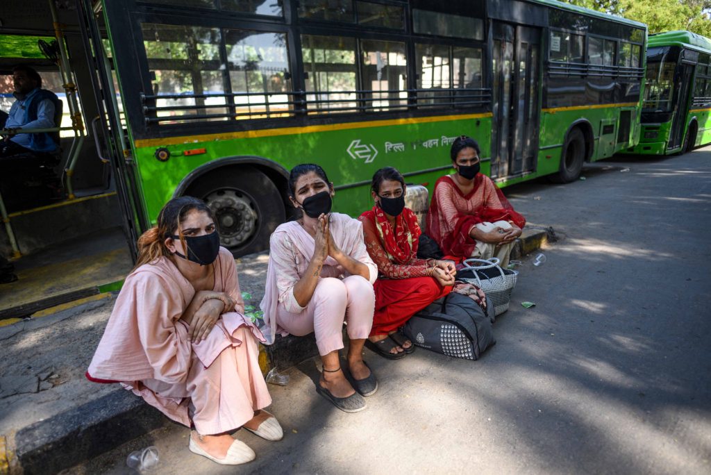 Four transgender people sit together, one looks as though they may be pleading for money. They are all four wearing facemasks.