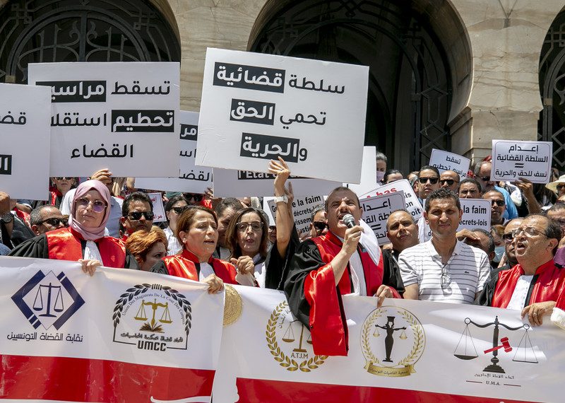 Protesters wearing red and white hold placards and banners with legal symbols.