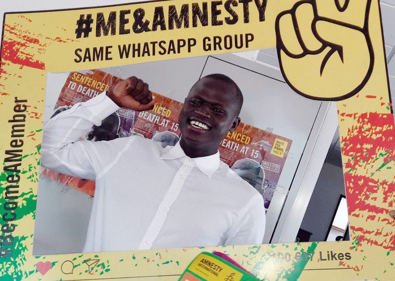 Young man holds up his fist in victory with a big smile on his face. He's surrounded by a colorful #Me&Amnesty frame.