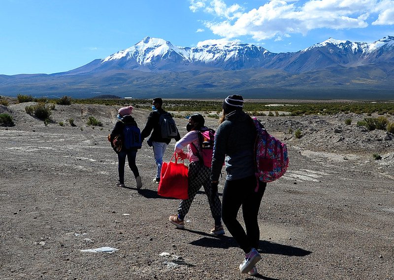 People walking, carrying their belongings with mountains in the distance.