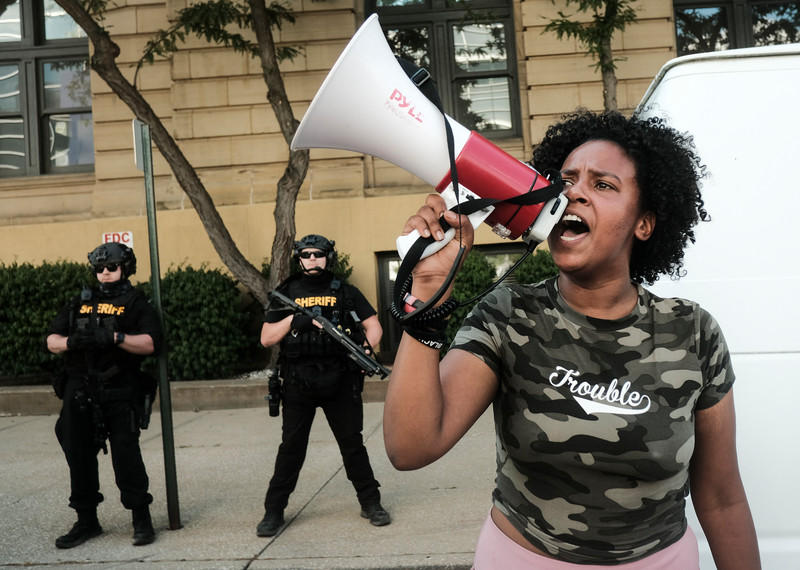 A person shouting with a megaphone whilst police officers stand in the background.