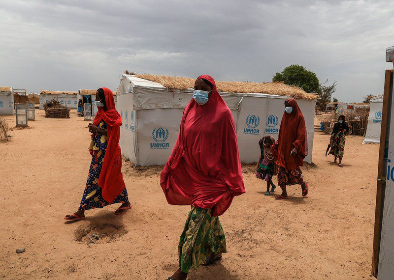 Women in red headscarves walk through a camp.