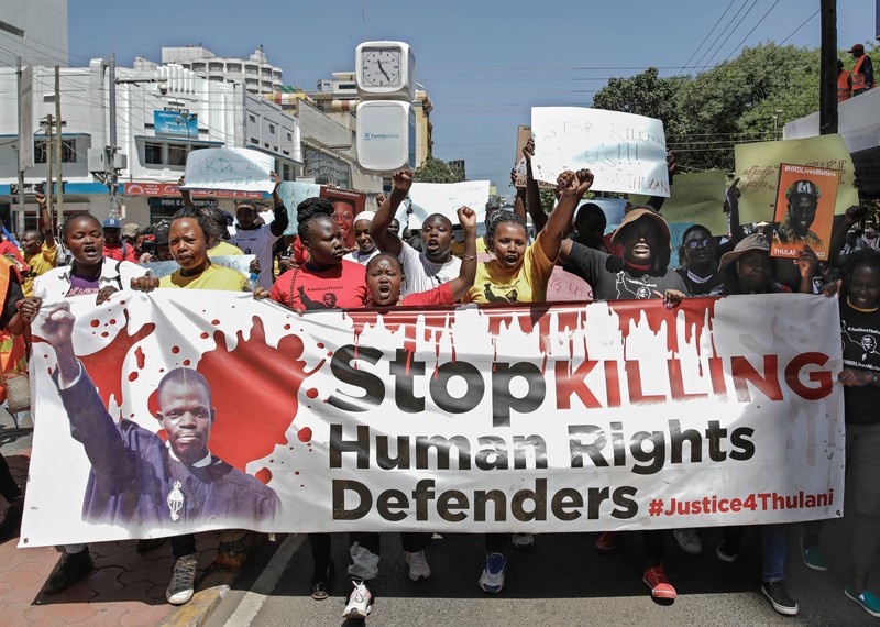 Protesters march holding a large banner which reads: 'stop killing human rights defenders'.