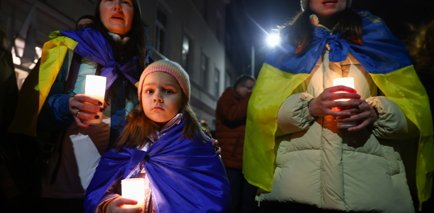 Girls with Ukraine flags around their shoulders hold candles