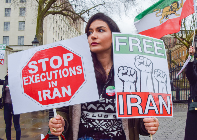 A woman holds two placards reading 'stop executions in Iran' and 'free Iran'. 
