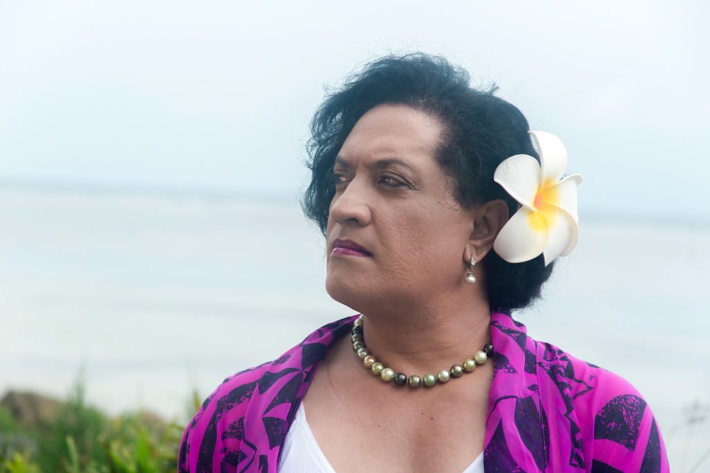 A portrait of Joey as she stands near the sea. She is wearing a white and yellow flower in her hair.