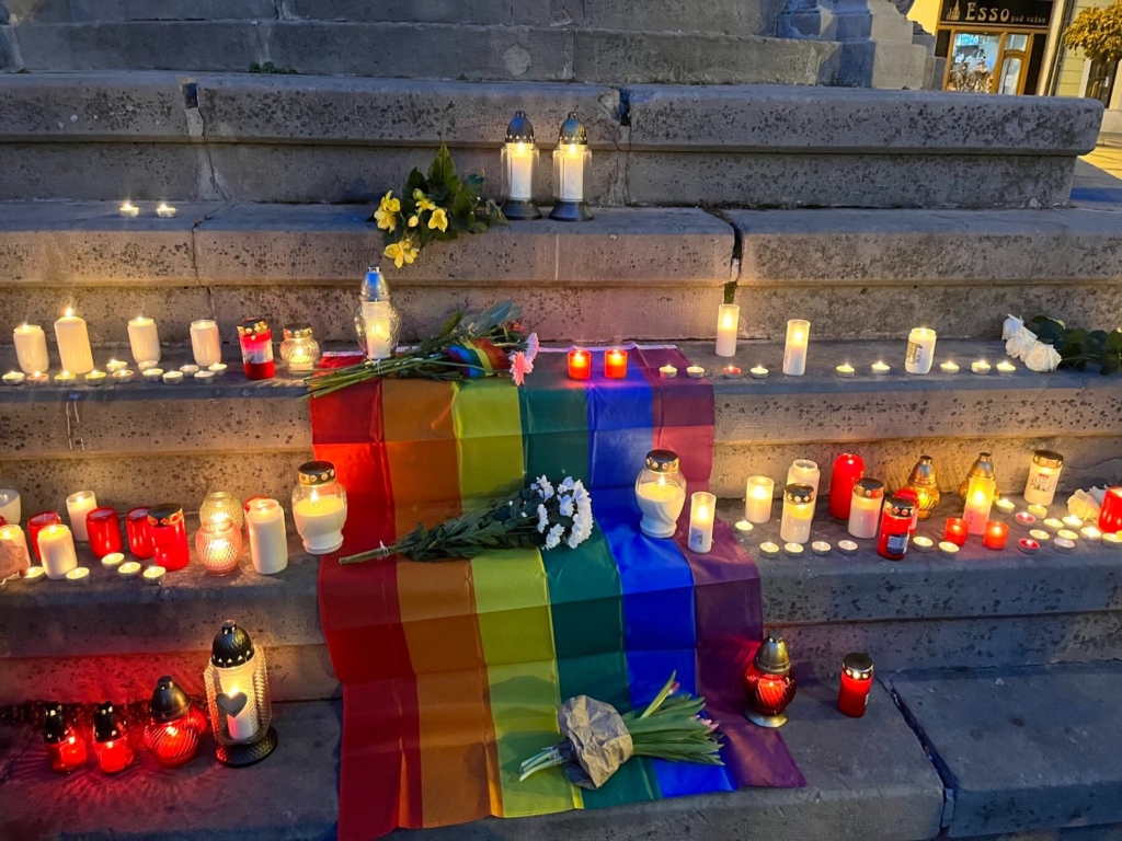 a rainbow lgbti flag is laid across a set of stairs. The flag is surrounded by candles and marks a vigil for people who were killed in an anti-LGBTI attack in slovakia