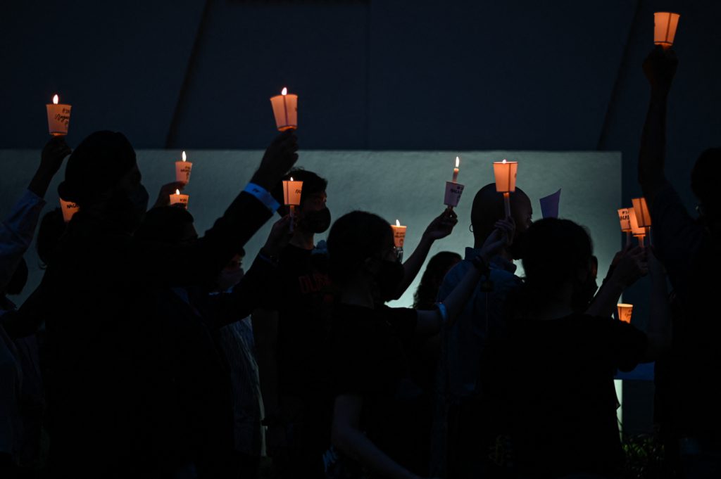 a group of people hold up candles at a vigil.
