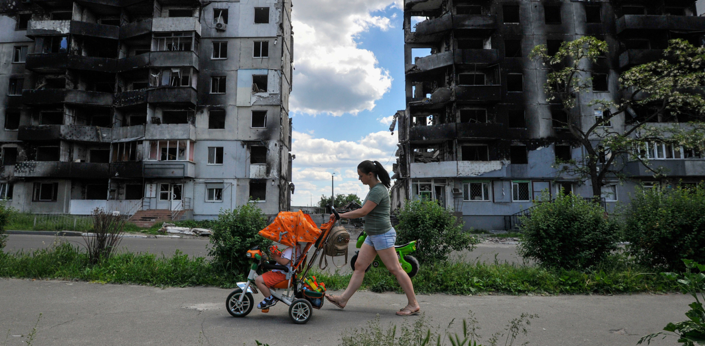 A woman with her child walks past a residential area that has been bombed.