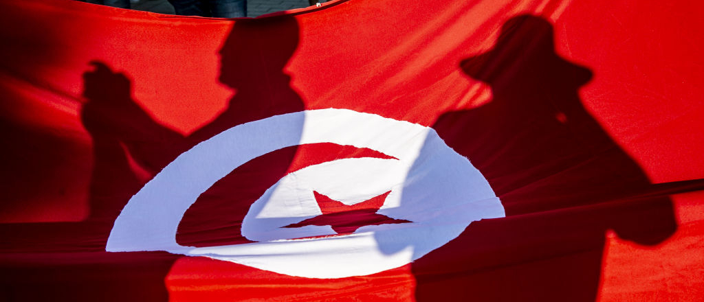 Shadows of Tunisians reflect on a Tunisian flag.