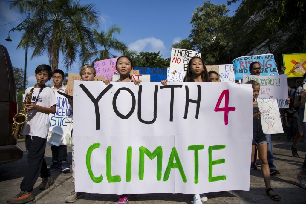 Marching students in Bangkok hold banners reading Youth 4 Climate