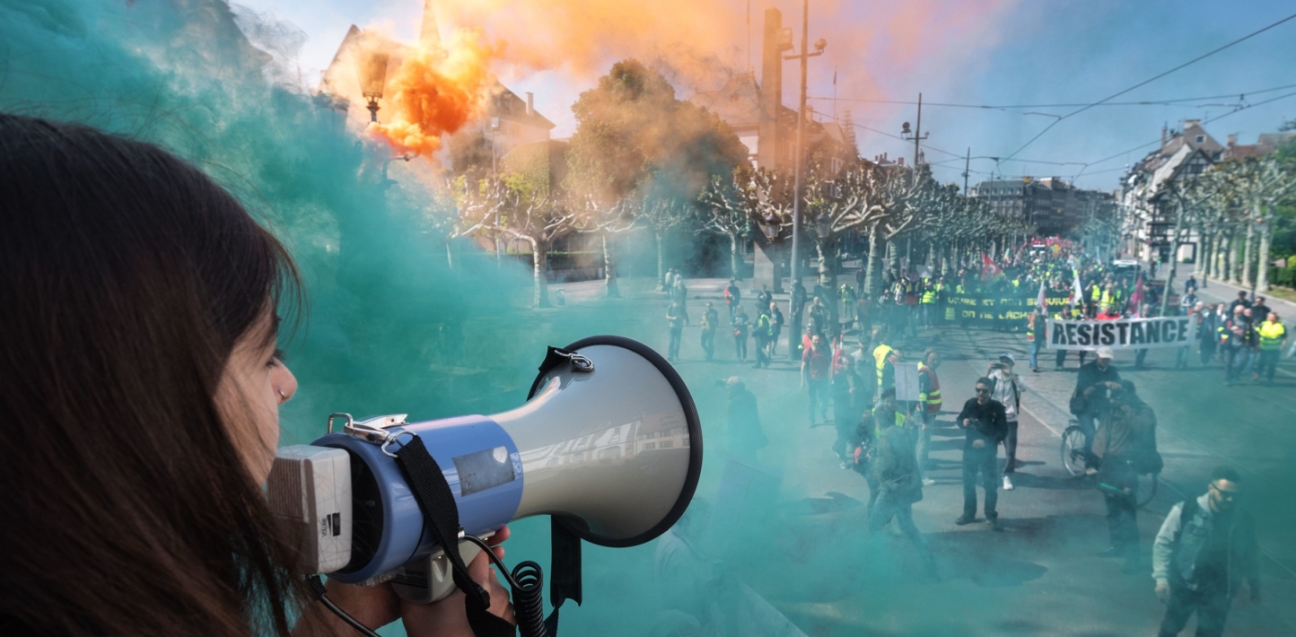 A protester speaks through a megaphone as smoke from coloured smoke bombs billows near people taking part in the annual May Day rally in Strasbourg, eastern France, on May 1, 2019.