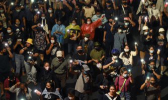 A crowd of protestors hold up phones their phones with the flash on.