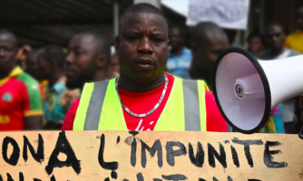 A man stands with a sign which reads 'non a l'impunite' alongside a megaphone.