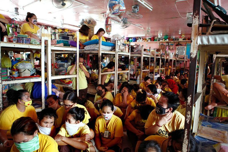 an overcrowded room in a prison in the Philippines. Apart from a few who sit on top bunk beds, people have nowhere to sit but on the floor. Some of them are wearing make-shift masks out of towels and shirts to protect them from covid-19.