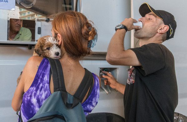 two patients stand at window where they can pick up medicine to treat drug addiction. One of them is holding a puppy and the other is drinking medicine from a white plastic cup.